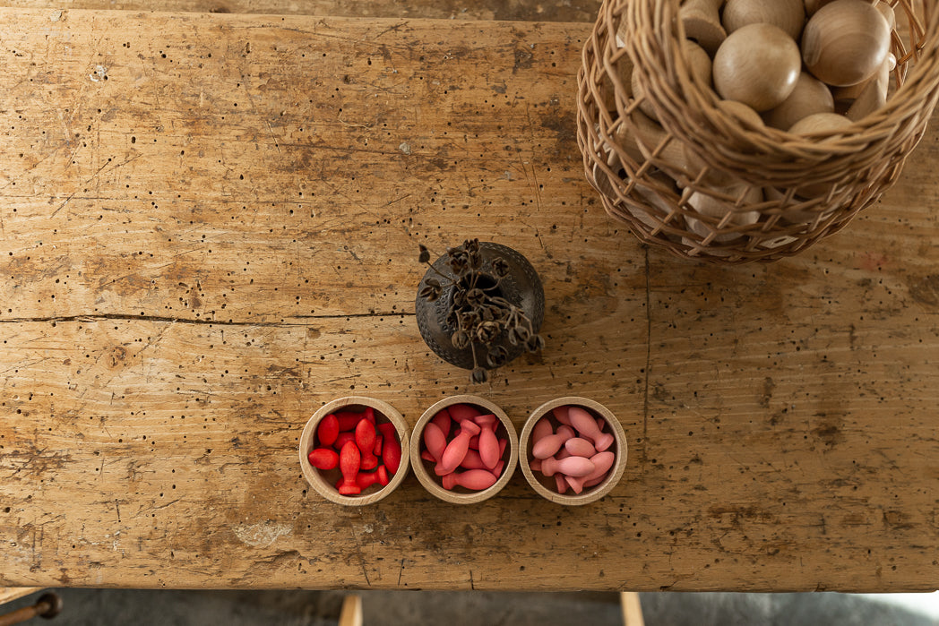 Pétalos de madera Grapat en tonos rojos y rosados dentro de tres cuencos sobre una mesa de madera